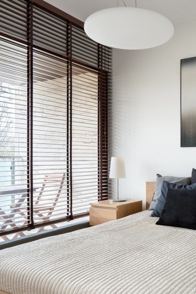 Modern bedroom with large windows covered by wooden blinds